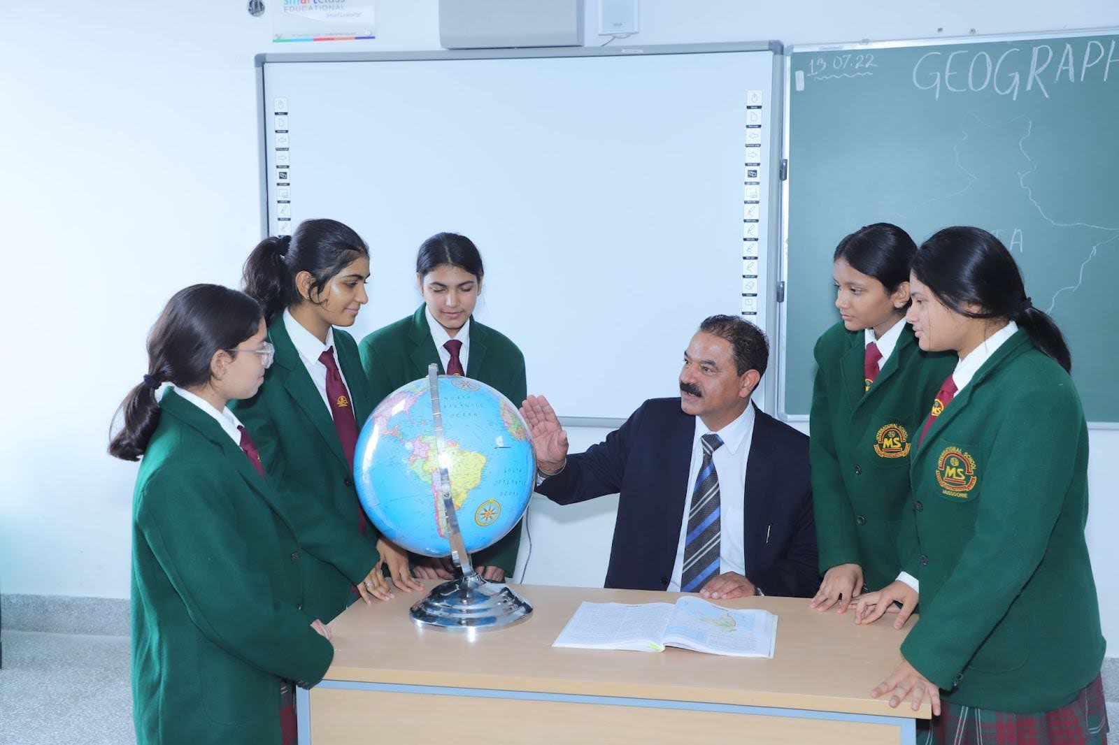 Sir teaches a group of girl students using a globe to explain world geography and global concepts in an interactive classroom setting.